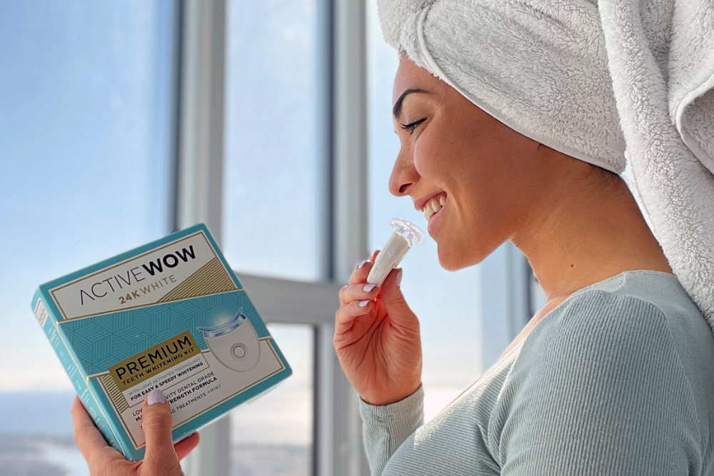 Young woman holding Active Wow Teeth Whitening Kit next to a window