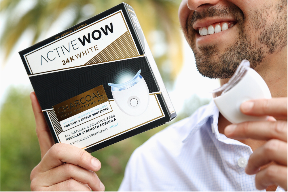 Young man holding Charcoal Teeth Whitening Kit near his face with an LED light in the other hand