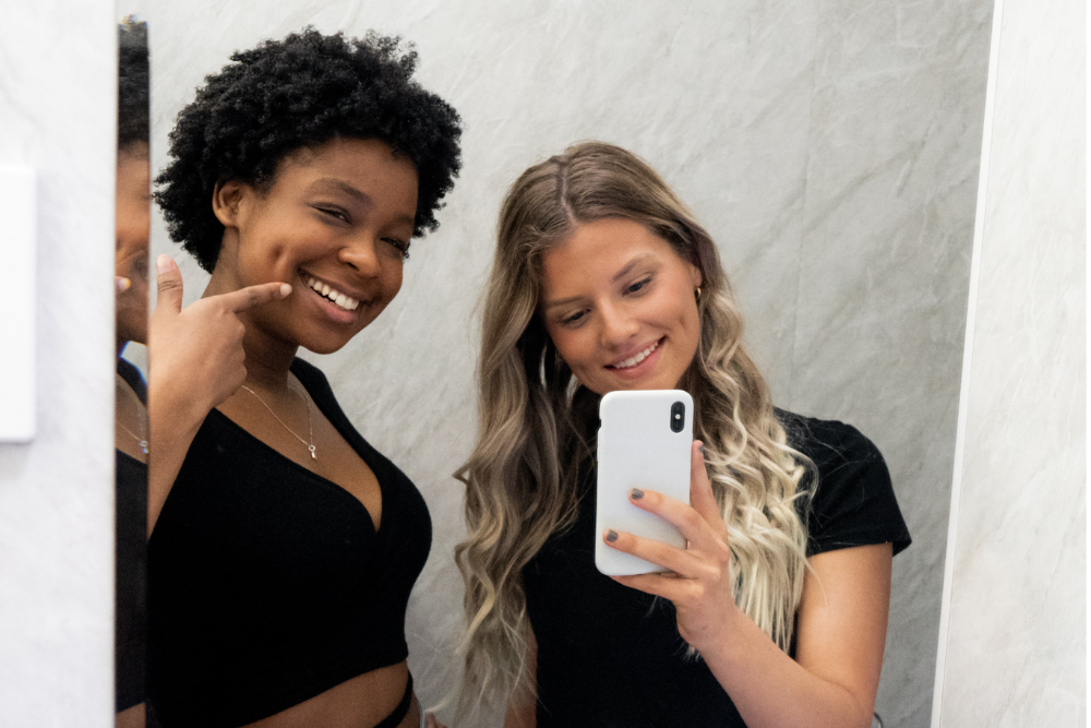 Two young women taking a selfie while looking in a mirror