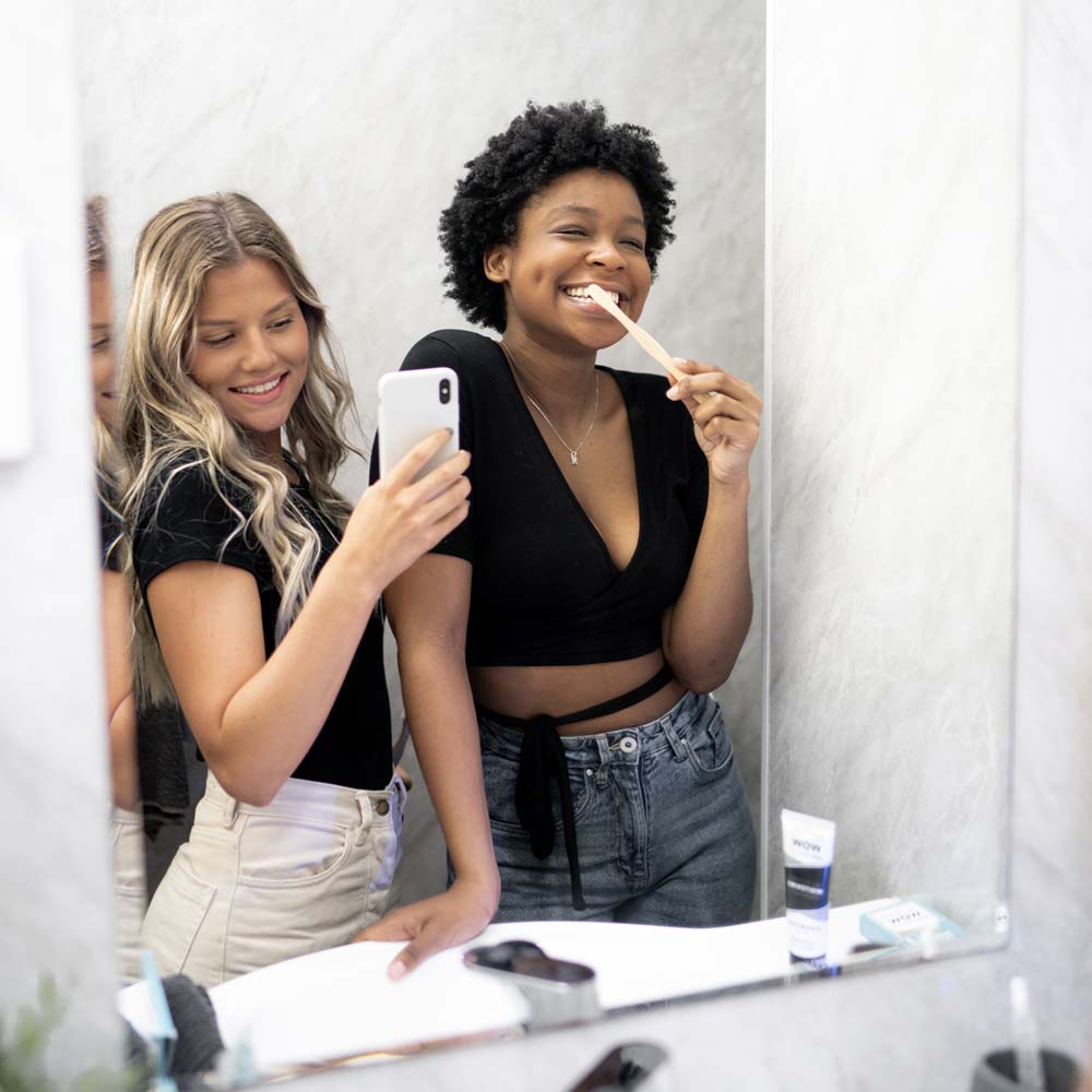 Two young women in the bathroom taking a selfie while brushing their teeth