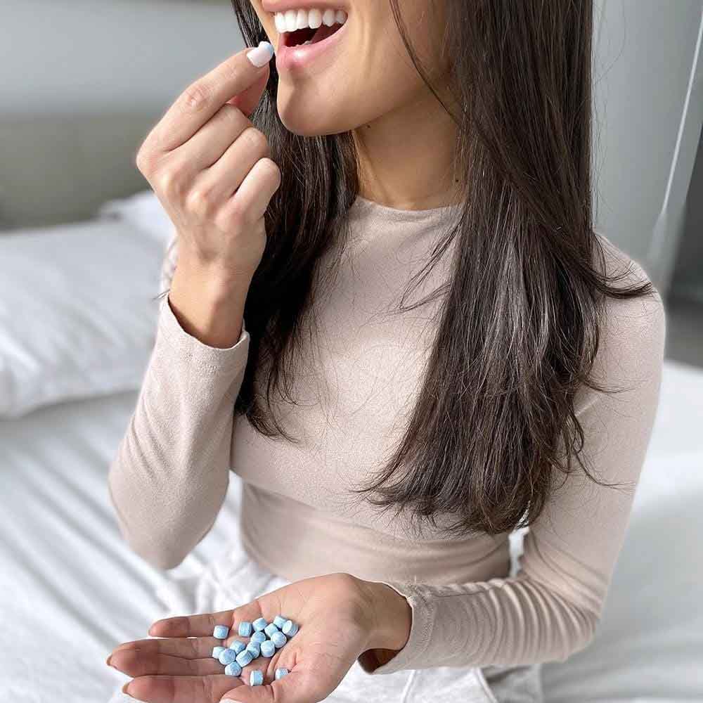 A woman holding Active Wow Natural Mouthwash Tabs in her hands as she puts one tab in to her mouth